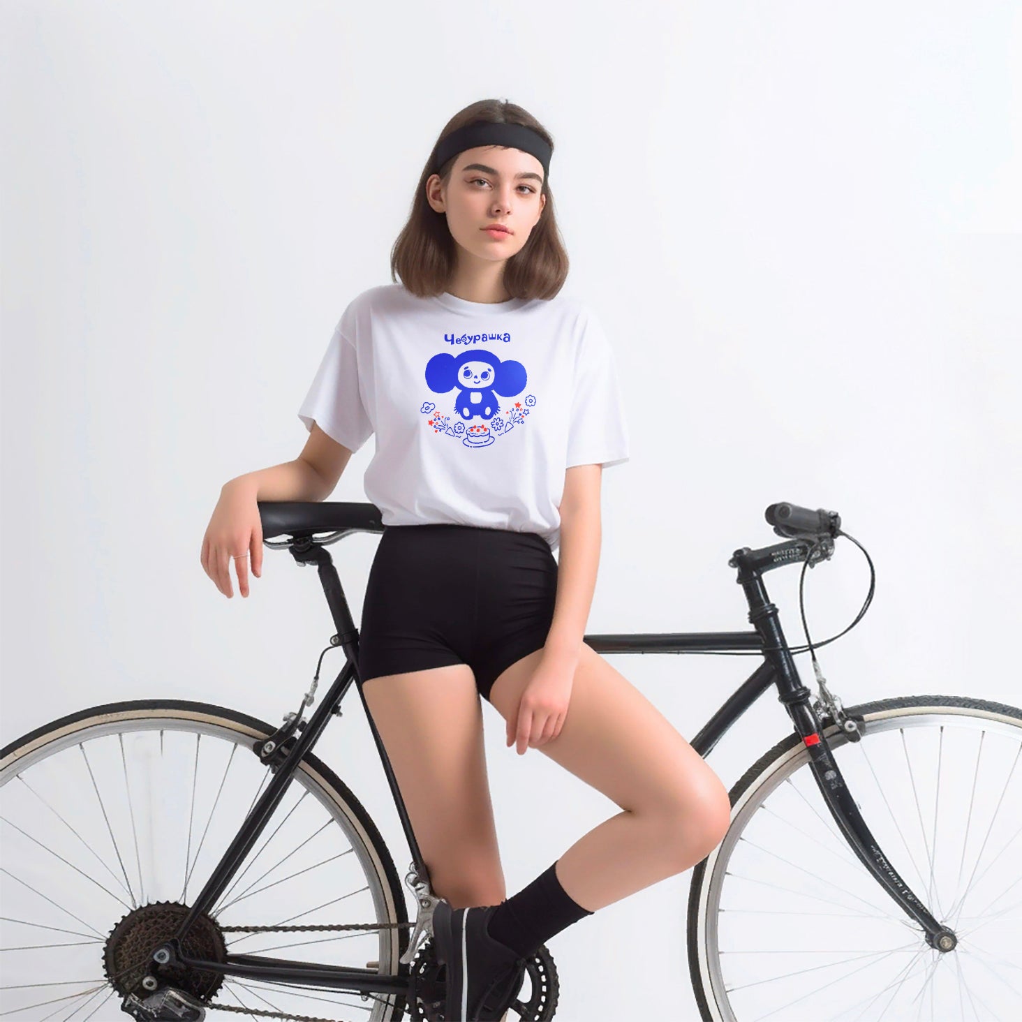 Cute Cheburashka with a birthday cake on a white T-Shirt worn by a young model girl in short shorts next to a bicycle